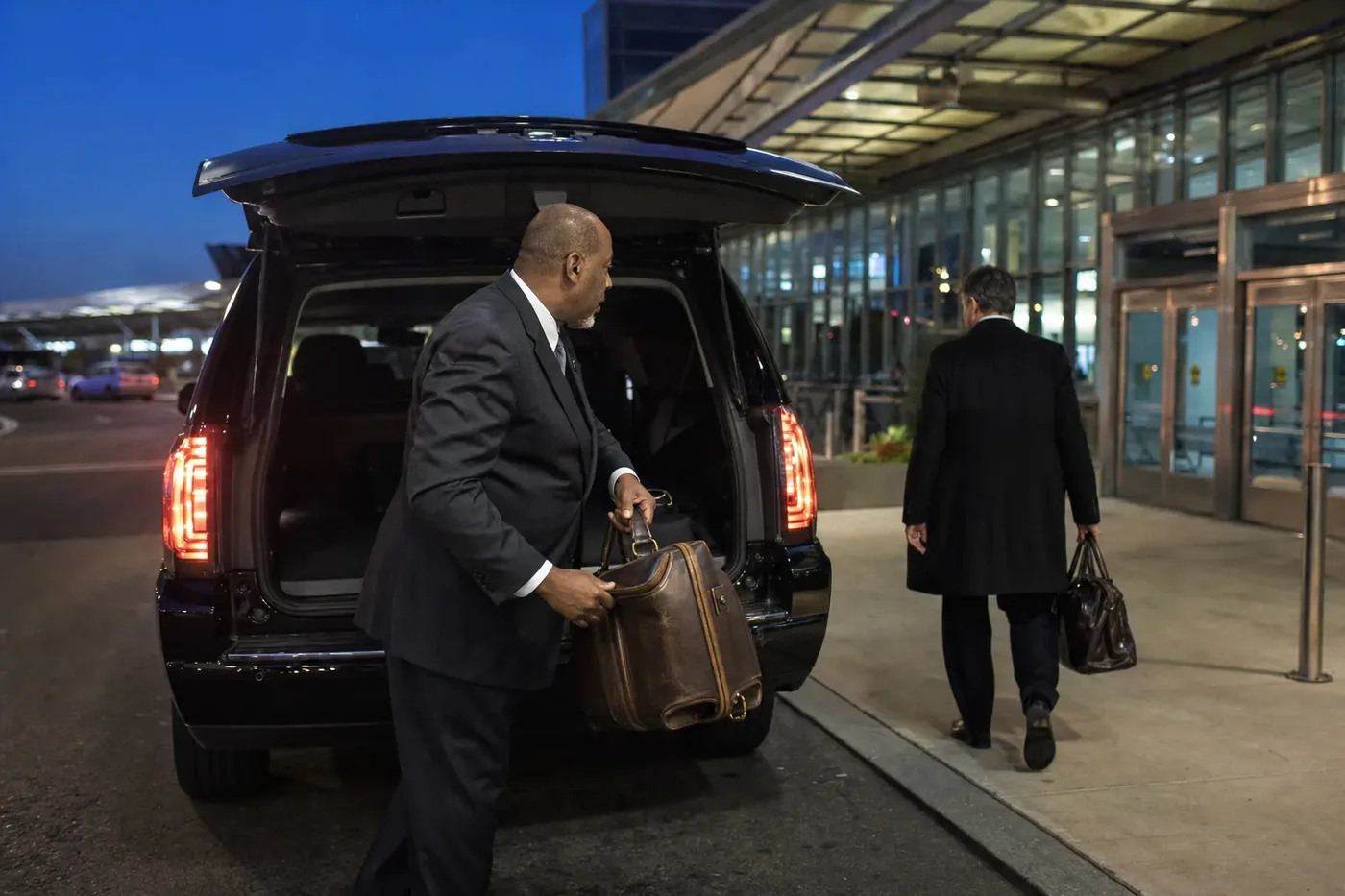 Business traveler stepping toward a lit terminal at dusk after a chauffeured departure transfer