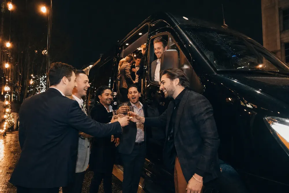 Groomsmen toasting beside a black Skyhawk Limousine party bus on a DC street at night
